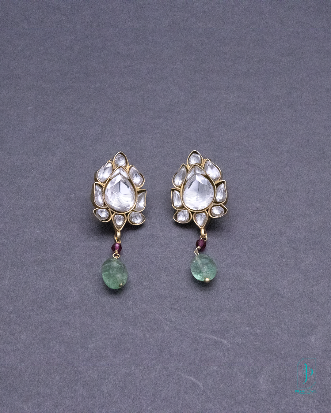 Pair of gold earrings with clear gemstones and green beads on a gray background